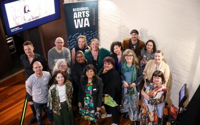 Regional Arts WA team with Regional Arts Network representatives and special guests. A photo of a group of arts workers smiling and looking at the camera with a sign with the text 'REGIONAL ARTS WA'.