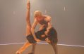 A sequence from Rafael Bonachela’s 'Somos', which is featured in Sydney Dance Company's 2025 season. A female dancer, long dark hair cascading towards the floor, holds one leg up in a sharply vertical position as she falls back into a shirtless male dancer's arms.