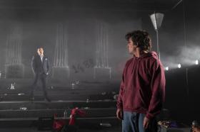 Two men, look across at each other on the set of 'Werewolf'. One in a suit, one in casual street gear. The steps the are standing are full of graffiti and rubbish.