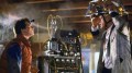 Michael J Fox, a young man in a red puffer jacket and Christopher Lloyd, with a contraption on his head as well. They are both attached to a machine in the middle in a scene of 'Back to the Future.'