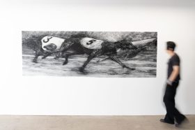 A man is standing beside a black and white painting of a racing greyhounds.