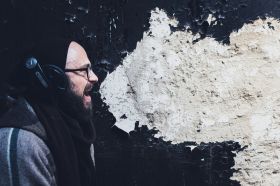 This week's arts news headlines and most read ArtsHub stories. A bearded man with glasses and wearing headphones shouts or sings beside a wall: the wall's peeling pain looks like a cartoon speech bubble.