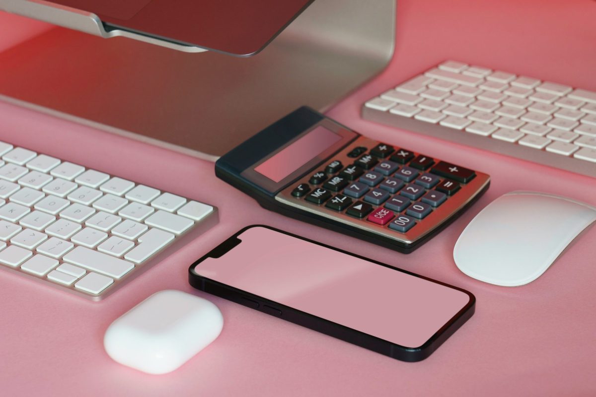 Keyboards, a mobile phone and a calculator lying on a pink surface.