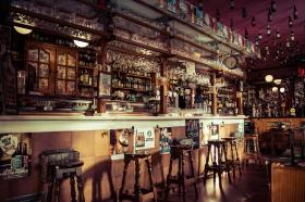 A bar, with stools and lots of bottles and shelving.