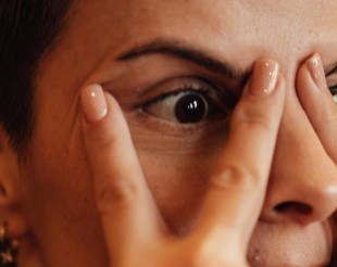 Woman covering her face and peeking through fingers. Arts news.