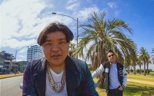 Brendan Wan and Randy Adeva, two young man in street gear standing outside in front of a palm tree.