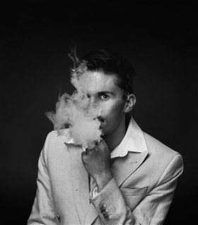 A black and white photo of magician, Lachlan Wilde. There is smoke covering his face.