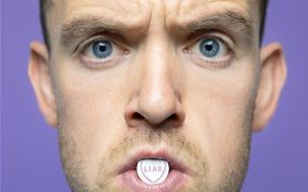 Close up face of a man, Tom Moran. He has a lolly with the word 'liar' on it in his mouth.