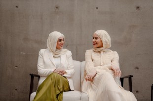 Two young women in white loose clothing and veils on their heads looking at one another.