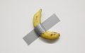 Installation view of Maurizio Cattelan's 'Comedian', 2019, on display in NGV Triennial 2023. A single banana duct-taped to a white wall.