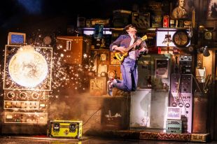 'Back to the Future: The Musical', original Broadway cast. A young man leaps into the air while playing an electric guitar, accompanied by a blaze of sparks.