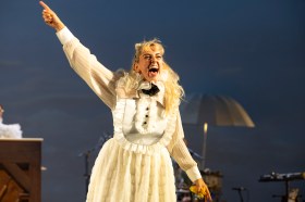 A woman with bleached blonde hair and 19th century clothing is shouting with her right arm raised. My Brilliant Career.