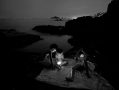 Black and white image of young boys at night lying on a rock near the sea with mobile phones with lit screens. Antonio Denti