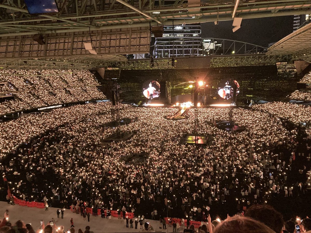 A concert stadium arena with thousands of people wearing light up wristbands. Coldplay