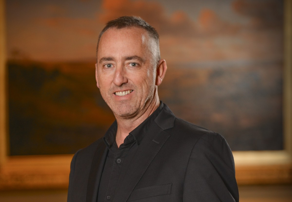 man in black suit smiling in front of abstract landscape painting. Jason Smith