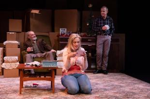 Geoff Kelso, and old man in shades of brown is seated in an armchair, Tegan Mulvany a blonde woman in jeans is kneeling on the ground.and Steve Turner is standing on the right hand. He is also dressed casually in this production of 'The Seed".