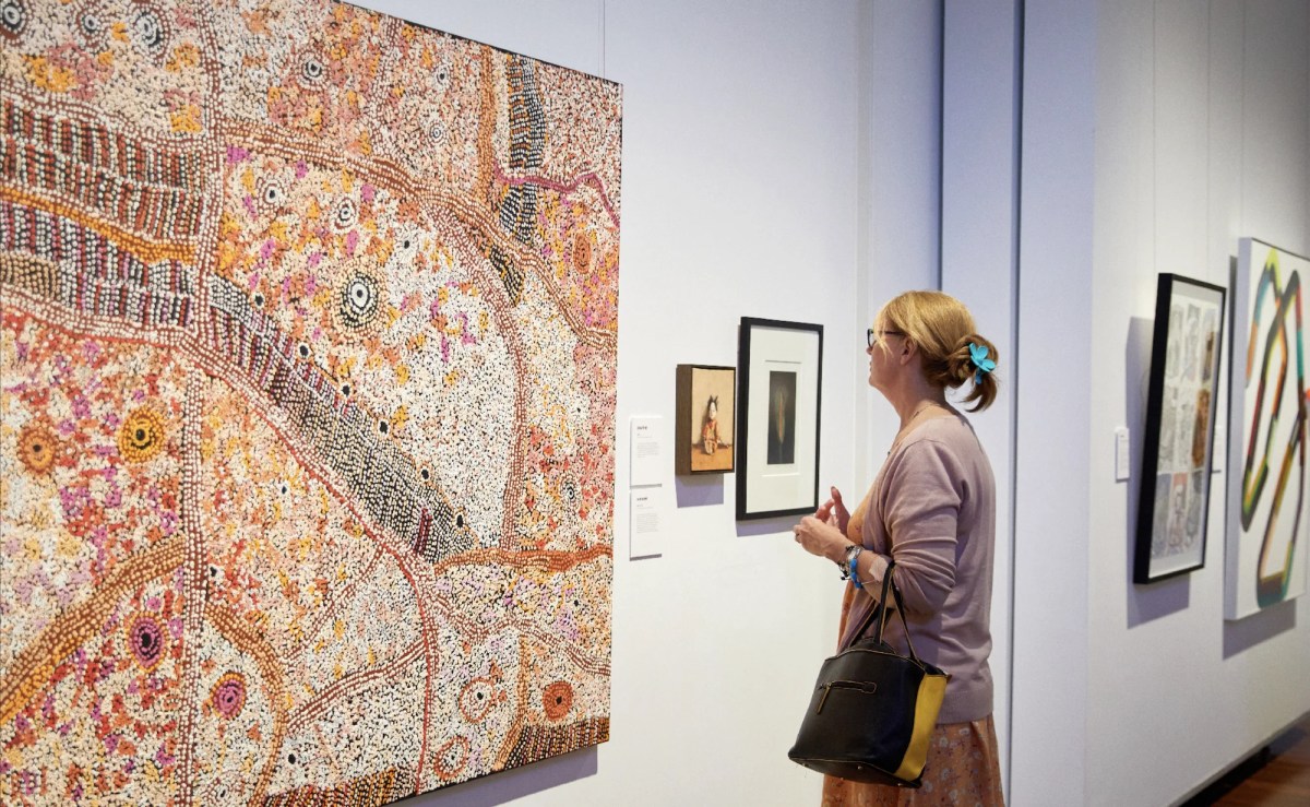 Young woman with blonde hair looking at Aboriginal painting in gallery. Muswellbrook prize