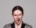 A publicity image for ACT Hub's 2025 season opener, 'Mojo' by English playwright Jez Butterworth. A dark-haired young man with fair skin holds a sword in front of his face. One side of his face is stern and impassive, the other side shows his eye and mouth wide open, as if shouting.