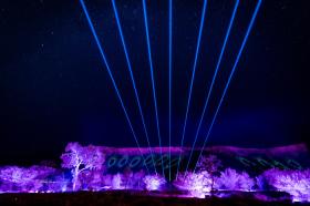 A light show with blue and purple colours is show against a mountain range.