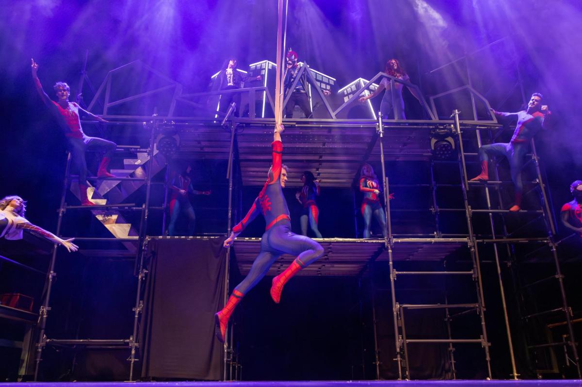 Several performers are dressed as Spider-men and are hanging off scaffolding.