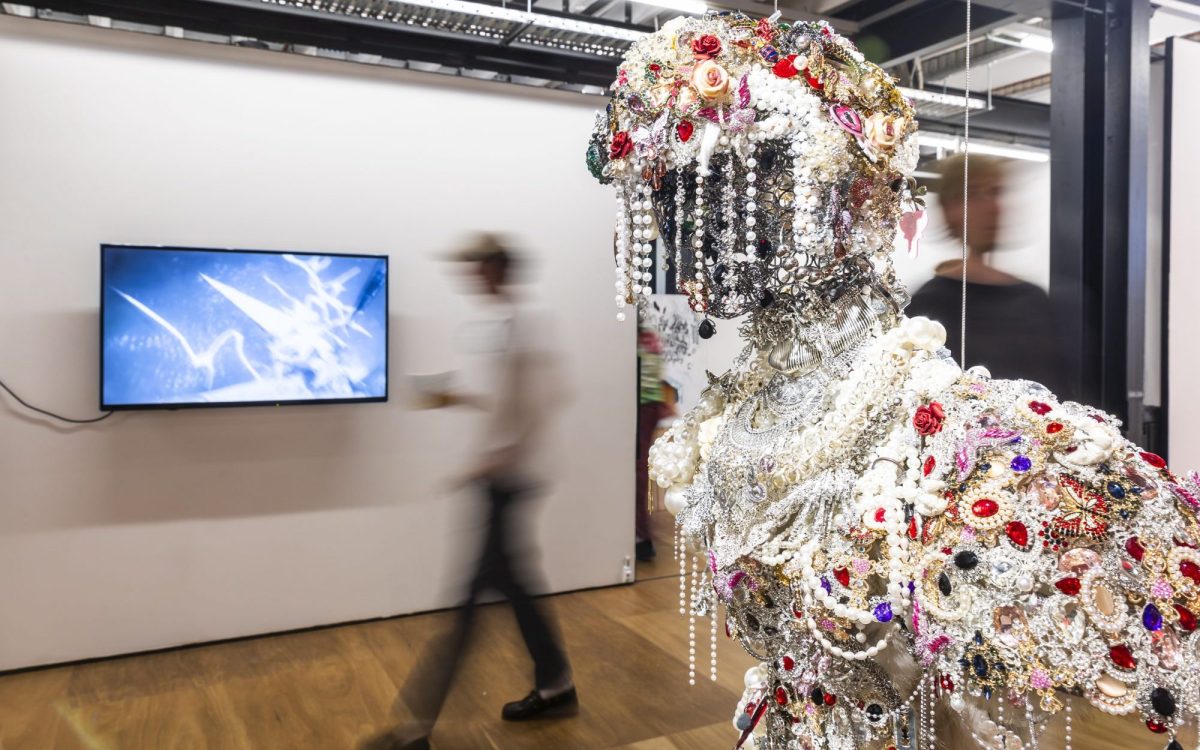 2024 VCA Grad Show, installation view, featuring graduate artists. On the right is a hovering sculpture with plastic pearls and jewels, vaguely representing a human figure. In the background to the left is a video work.