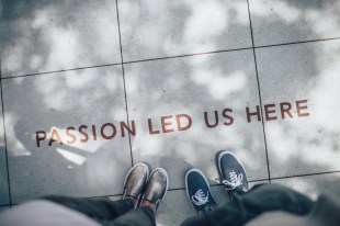 Two sets of feet standing on a pavement, on which is written in red 'passion led us here'. portfolio career in the arts