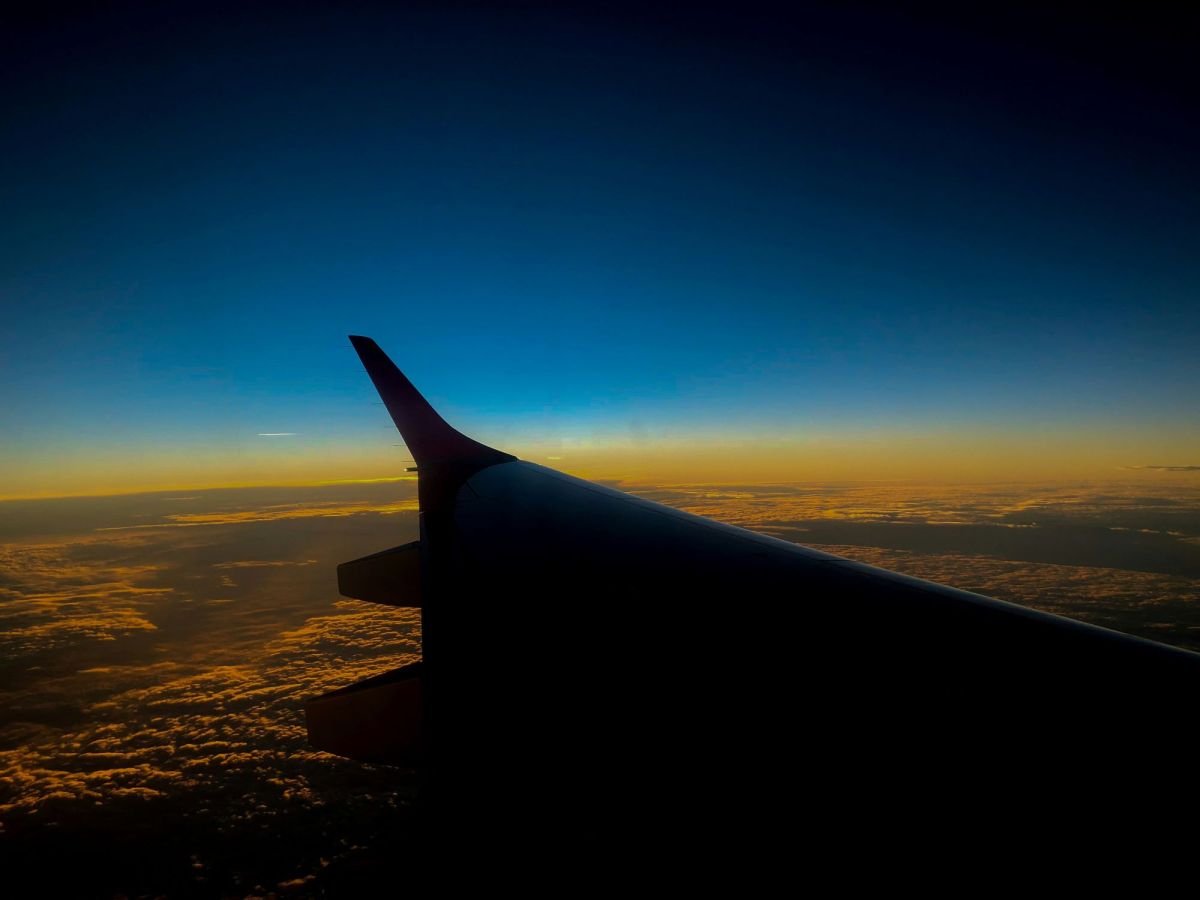 On the Move is ArtsHub's weekly round-up of Australian arts sector comings and goings. The photo shows a plane in flight, high above the clouds, focusing on the plane's wing at evening and the last glow of sunlight in the darkening sky.