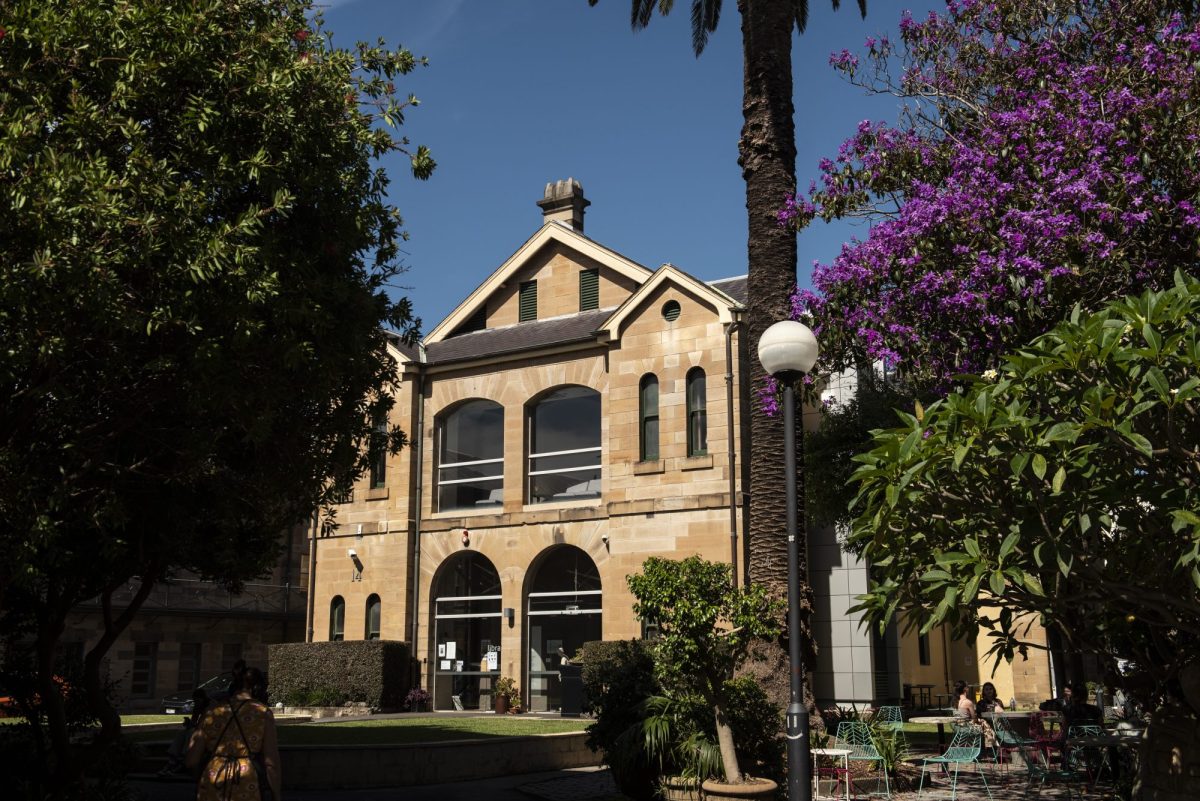 The exterior of an old two-storey sandstone building on a campus with trees around it. National Arts School.