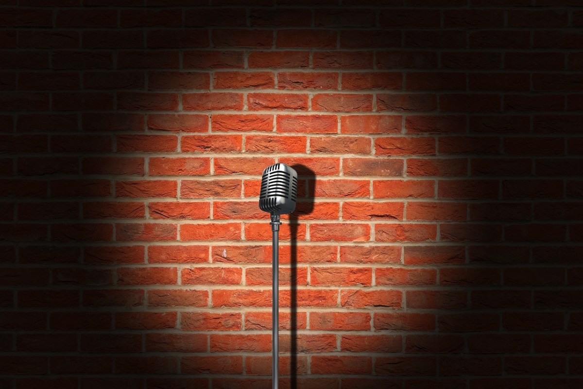 A spotlight on a brick wall and in the middle a stand with an old fashioned microphone. Comedy festival season.