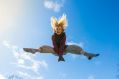 On the Move is ArtsHub's weekly round-up of arts sector appointments. The image shows a woman with long hair jumping in the aur. Her long hair flies up around her and her legs are outstretched. Blue sky and white clouds are visible behind her.