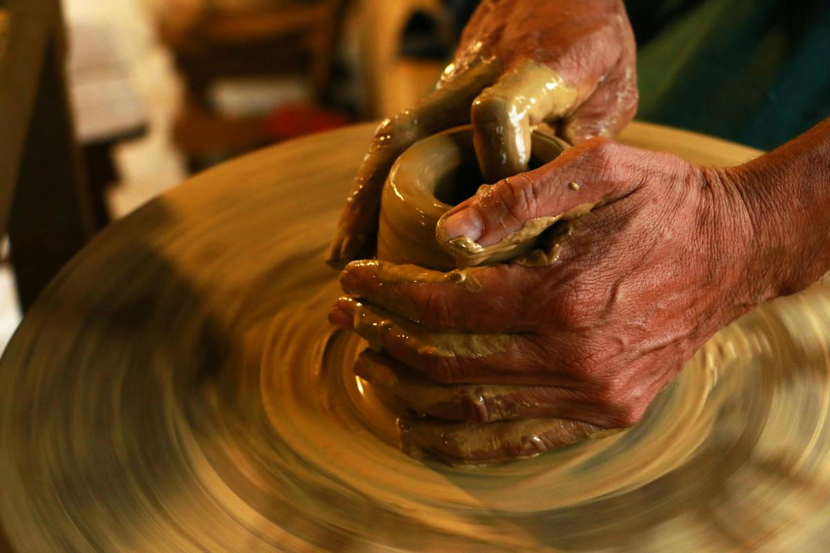 Older hands on a potter's wheel moulding some clay. workshop