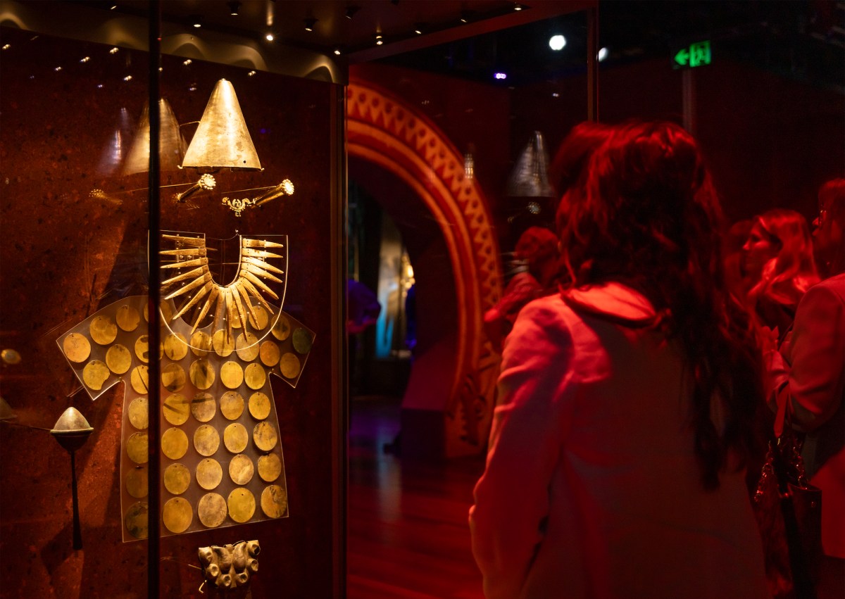 Woman in red lit gallery looking at ancient gold body ware. Machu Picchu