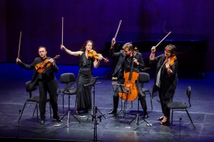 A string quartet wave their bows in the air on stage.