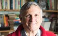 John Marsden, an man with grey hair and a red jumper smiling. There are shelves of books behind him.