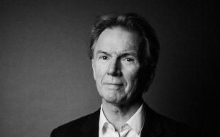 A black and white portrait photo of Peter Rose, outgoing editor of 'Australian Book Review.' He is an older Caucasian man wearing a white shirt under a dark jacket.