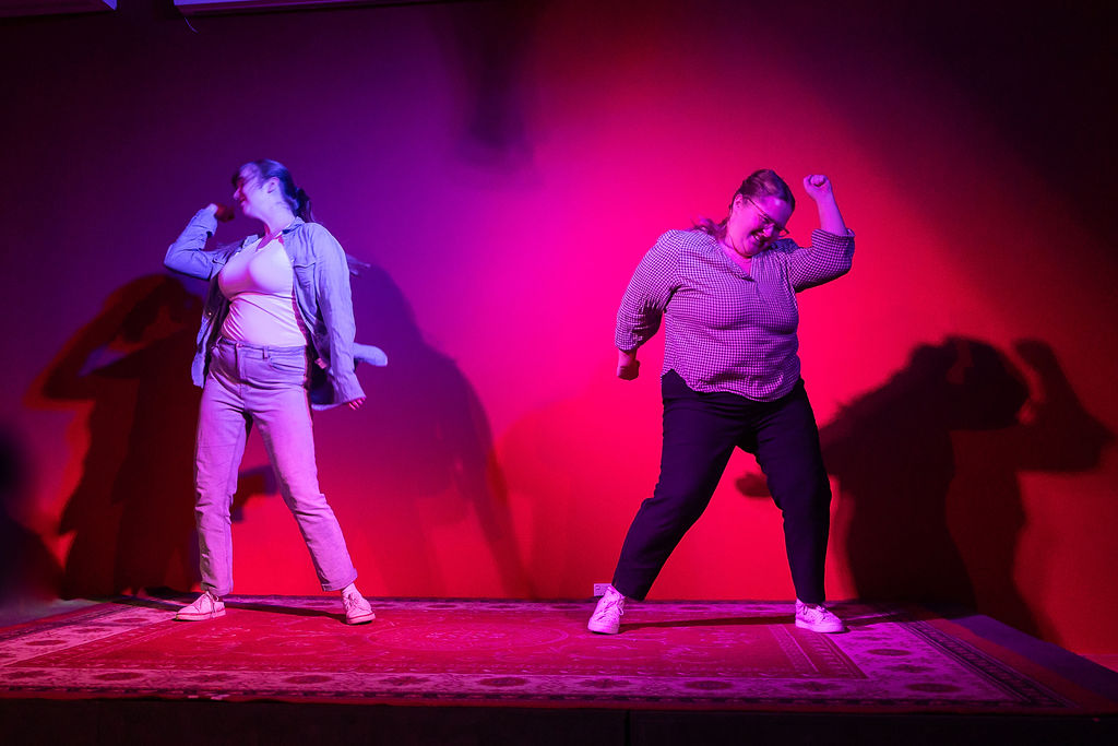 Two young women are dancing in 'Sauce". The lighting that falls on them is in tones of red. Sauce