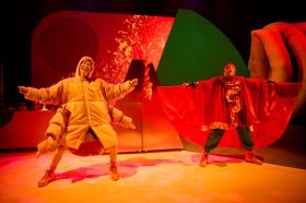 Windmill Theatre Co's 'Moss Piglet' is touring regional South Australia in 2025. Two actors in colourful costimes, one with eight limbs and another with wings, stand on a brightly lit set.