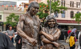 Uncle Archie Roach and Aunty Ruby Hunter have been immortalised in bronze in Fitzroy’s Atherton Gardens. The photo shows the two statues standing closely together and smiling.