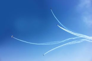 ArtsHub's On the Move column is a weekly round-up of career comings and goings in the Australian cultural sector. The photo shows four planes at an air show, each climbing in different directions against a blue sky and leaving smoke trails behind them.