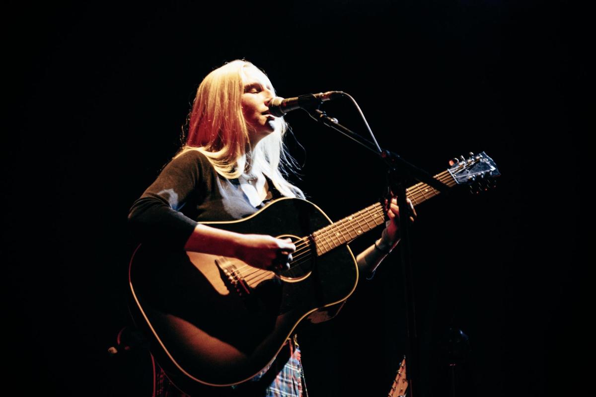 Billie Marten, a singer/musician who has long blonde hair. She is holding a guitar and singing.