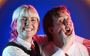 Bek Schilling and Sean Donehue in 'Bearded'. Shilling is on the left and has dyed platinum blonde hair with pink tips. Thye are mock playing and holding Sean Donehue's mouth open.