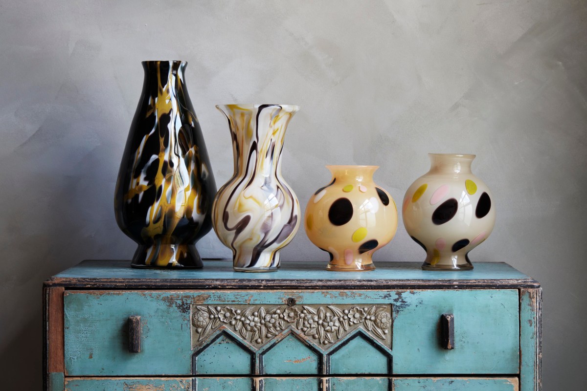 A selection of four glass vases with brown, yellow and cream swirling patterns and dots, set on a vintage looking cabinet with aqua paint. 