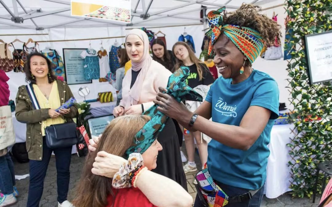 The Africultures Festival. A black woman tying a hair and on a white woman at the festival with people around them.