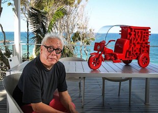 Asian man in black with black glasses and red Chinese bicycle sculpture in coastal setting. Laurens Tan