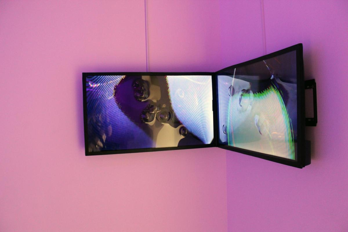 On a pink wall, two video screens are set next to each other.