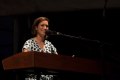 Photo of a Caucasian woman standing at the podium speaking into a mic.