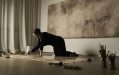 2024 Urbach recipient Ellen Lee, photographed inside a softly lit space where she is kneeling on the ground and working watery brown colours into a flat canvas.