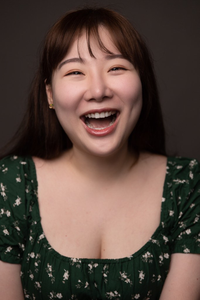 A long-haired young woman of Asian appearance in a low-cut dress is smiling with an open mouth. Stella Wu.