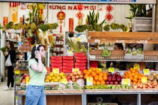 A teenager wearing headphones is walking past an array of fruit in a greengrocer store.