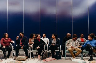 Group of people casually chatting in a row of chairs against a blue wall. Arts conference